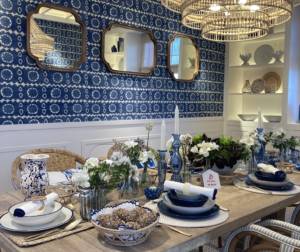 Diseño de interiores con mesa de madera, sillas en tonos marrones, blancos y grises, luminarias naturales de mimbre, pared azul con papel pintado, espejos y vajilla en tonos tierra con vegetación