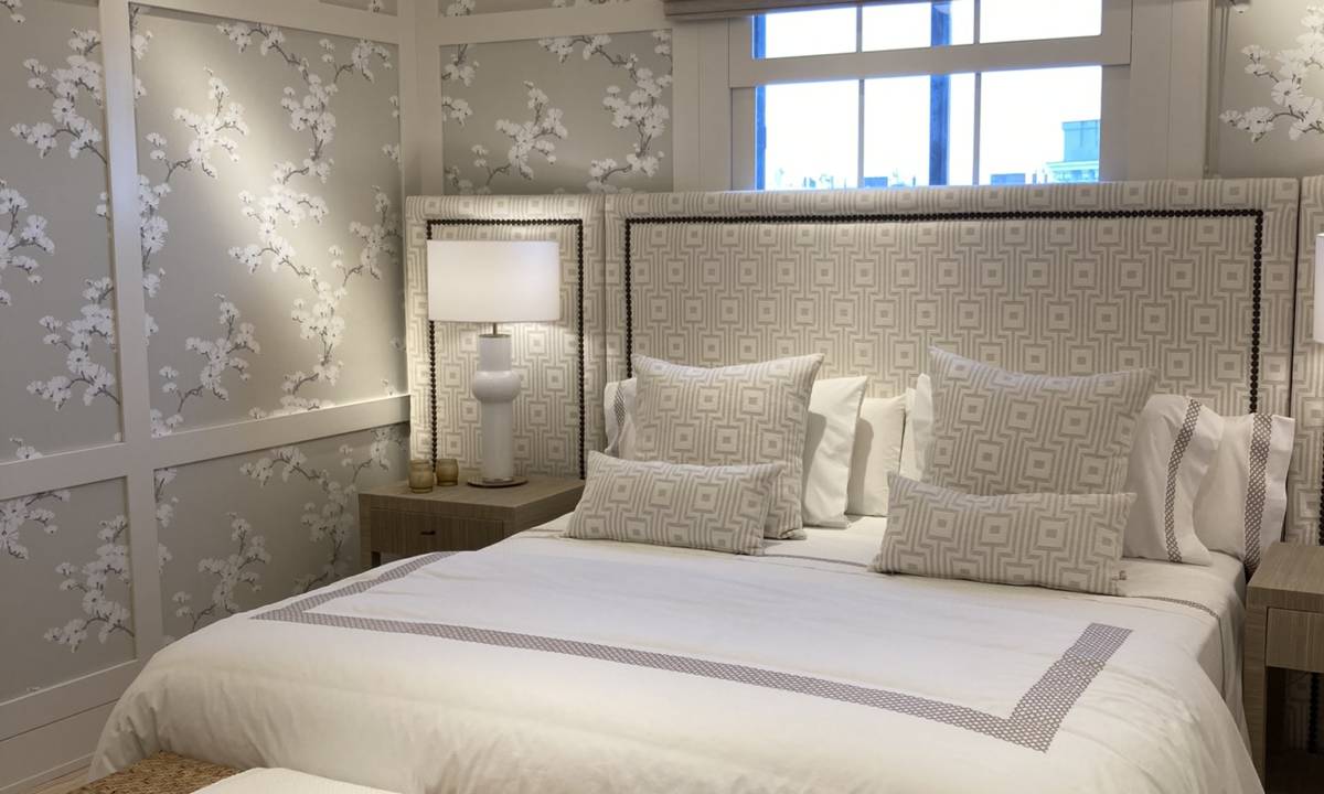 Insight_Casa Decor_Zona de dormitorio con tonos blancos, cama, cojines, asiento de mimbre, paredes con textura e iluminación