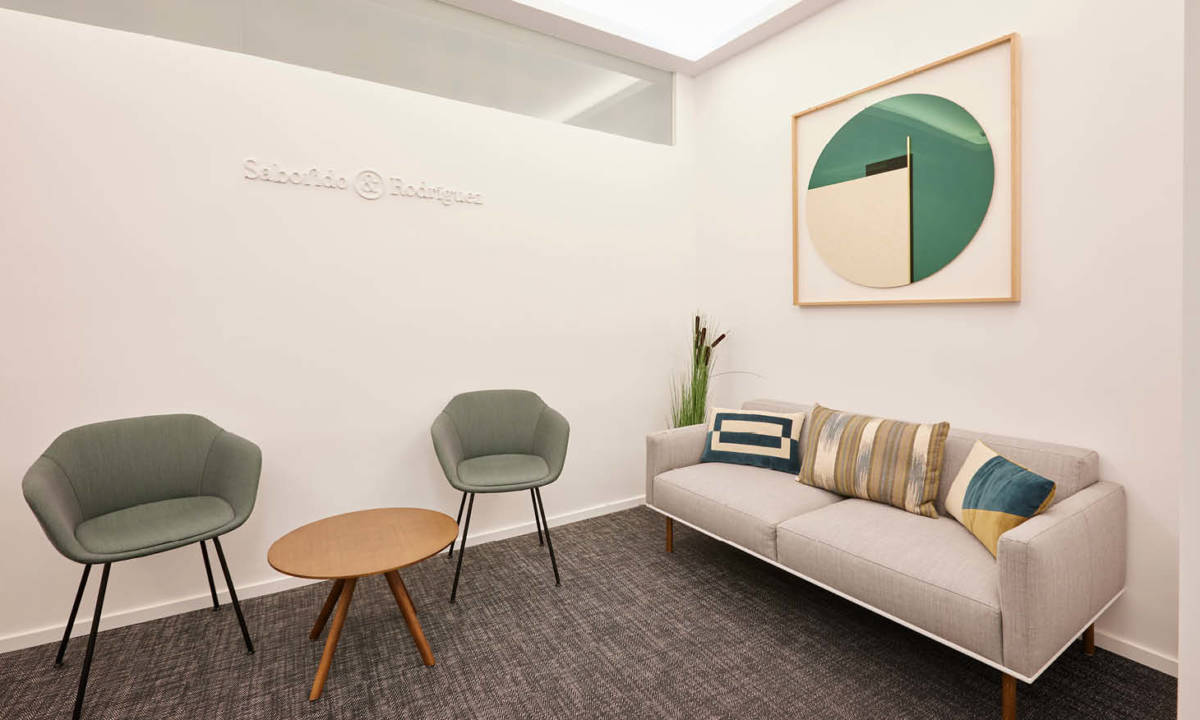 Zona de recepcion de clinica dental con sofas, cuadro y tonos verdes
