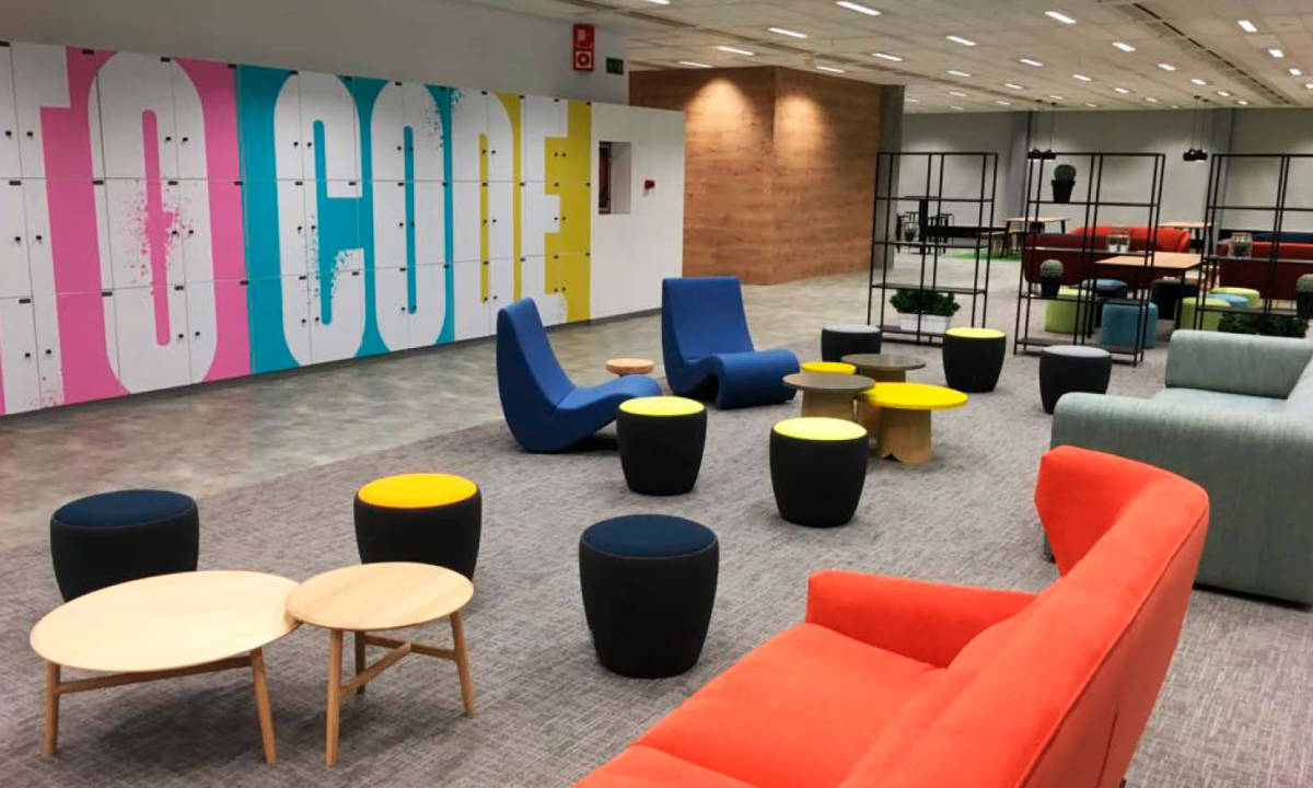 Zona común en espacio de oficinas con mobiliario moderno y colorido, taquillas, y espacio de socialización y descanso común para empleados