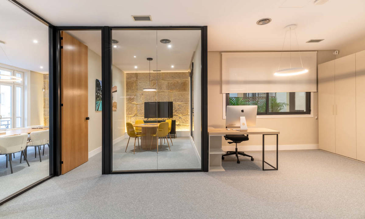 Zona de recepción y sala de reuniones divididas mediante compartimentación con mampara de vidrio y madera diseñada por Sutega