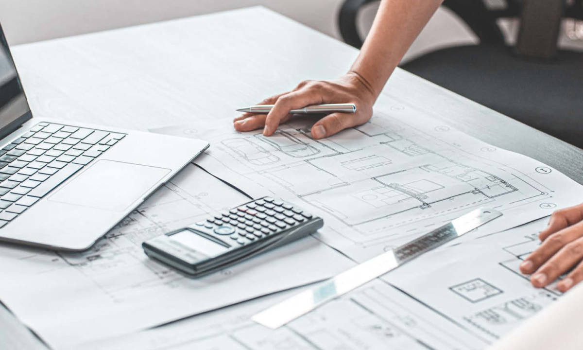 Técnico, arquitecto o ingeniero trabajando con planos y ordenador según metodología BIM, en una mesa de trabajo en oficina técnica