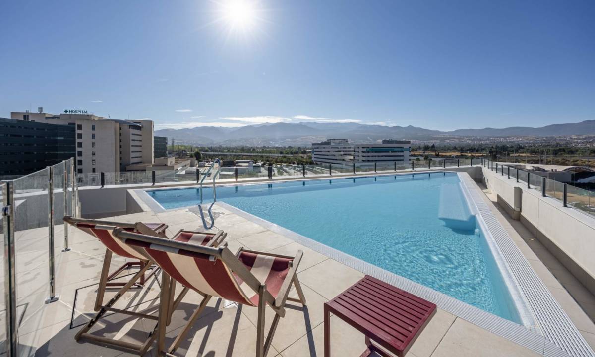 Espacio exterior de piscina en residencia de estudiantes con mobiliario de sillas, mesas y hamacas