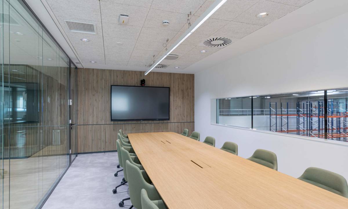Sala de reuniones con sillas tapizadas en verde, mesa de carpintería a medida y monitor de TV para videoconferencia