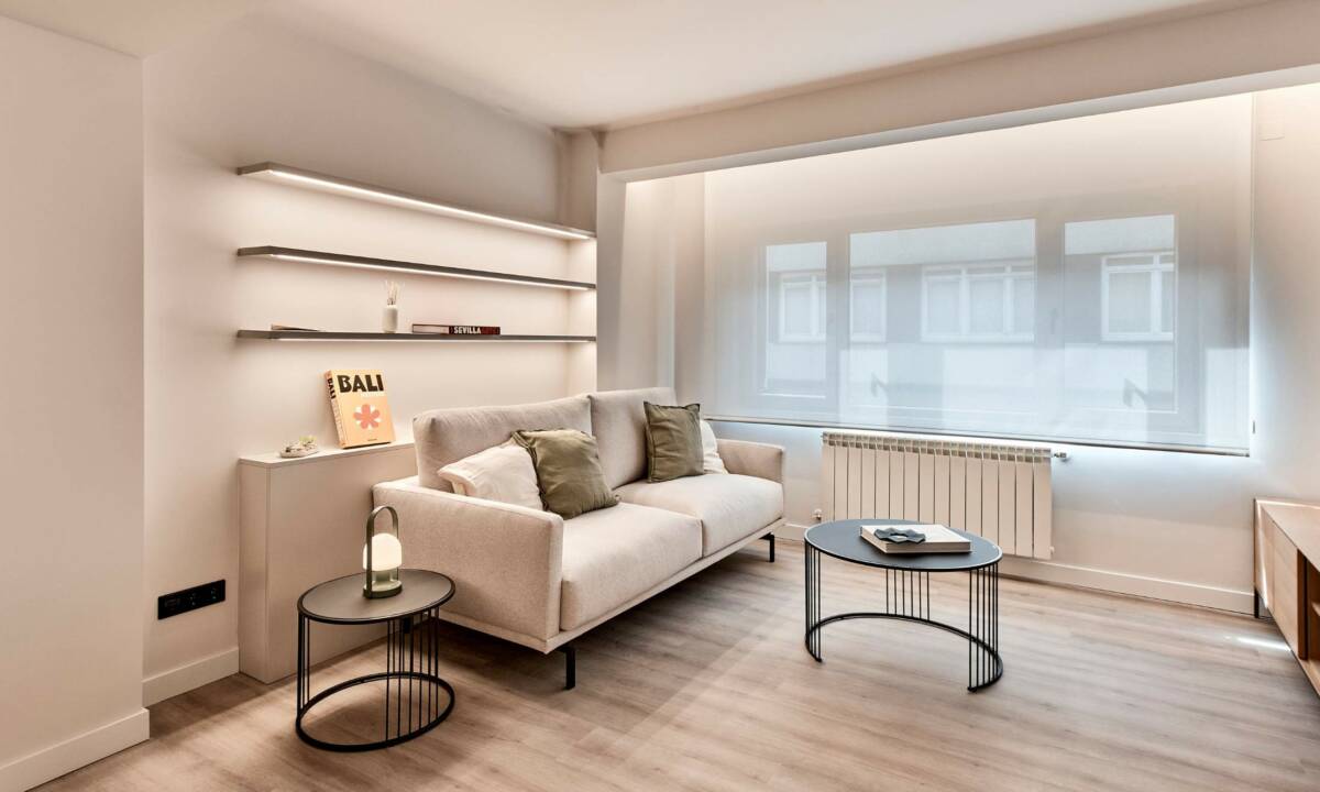 Sofá en salón, con mobiliario estándar y estantería a medida retroiluminada en salón espacioso con colores claros