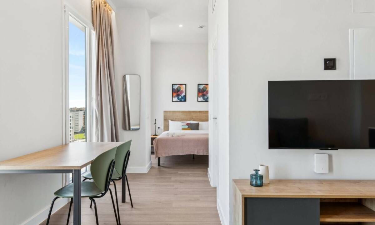 Zonas privadas de coliving en Madrid con estudio con cama doble, mesa con sillas y salón con TV