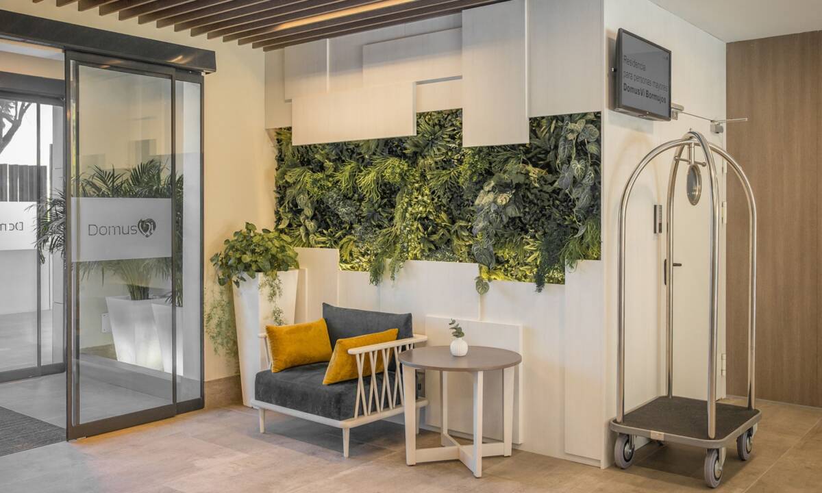 Zona de entrada a residencia de mayores con sofás en azul y amarillo y jardín vertical a medida decorativo