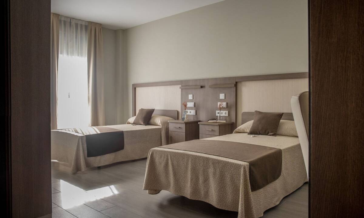 Habitación con dos camas en residencia de mayores con tonos beige y marrón