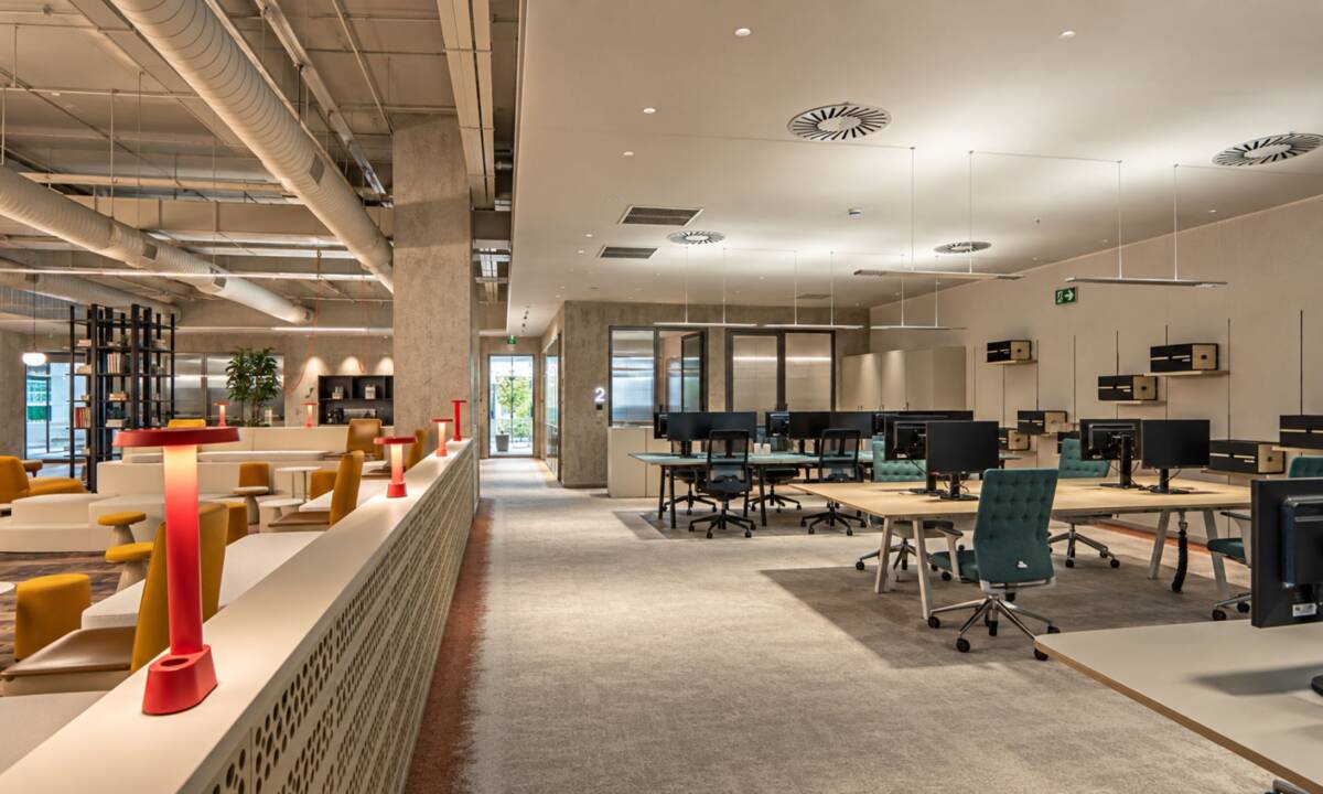 Espacio abierto de trabajo en oficina, con zona de ágora, puestos operativos y salas de reuniones compartimentadas