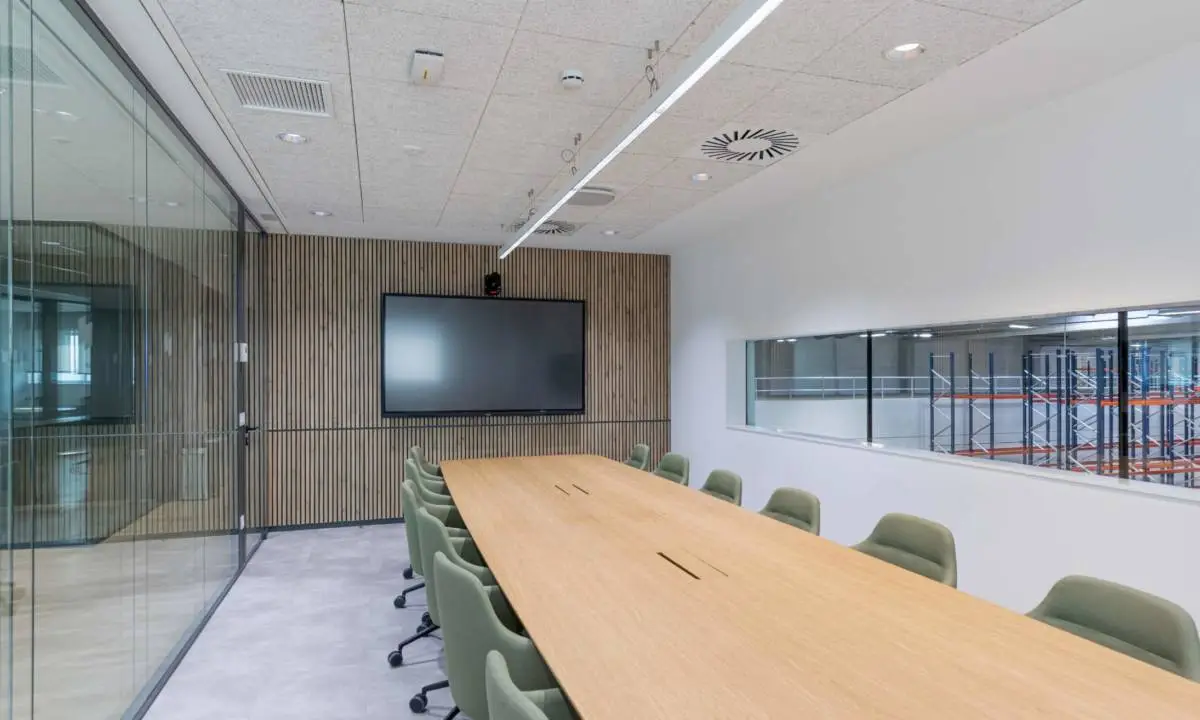 Sala de reuniones con sillas tapizadas en verde, mesa de carpintería a medida y monitor de TV para videoconferencia