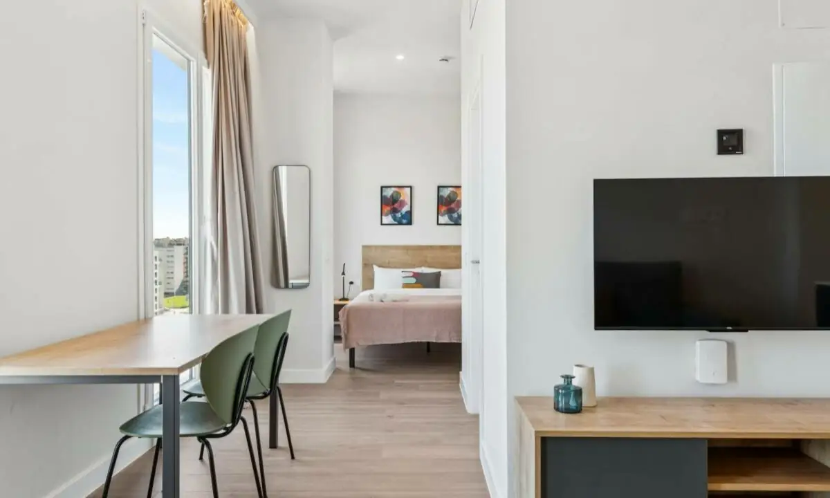Zonas privadas de coliving en Madrid con estudio con cama doble, mesa con sillas y salón con TV