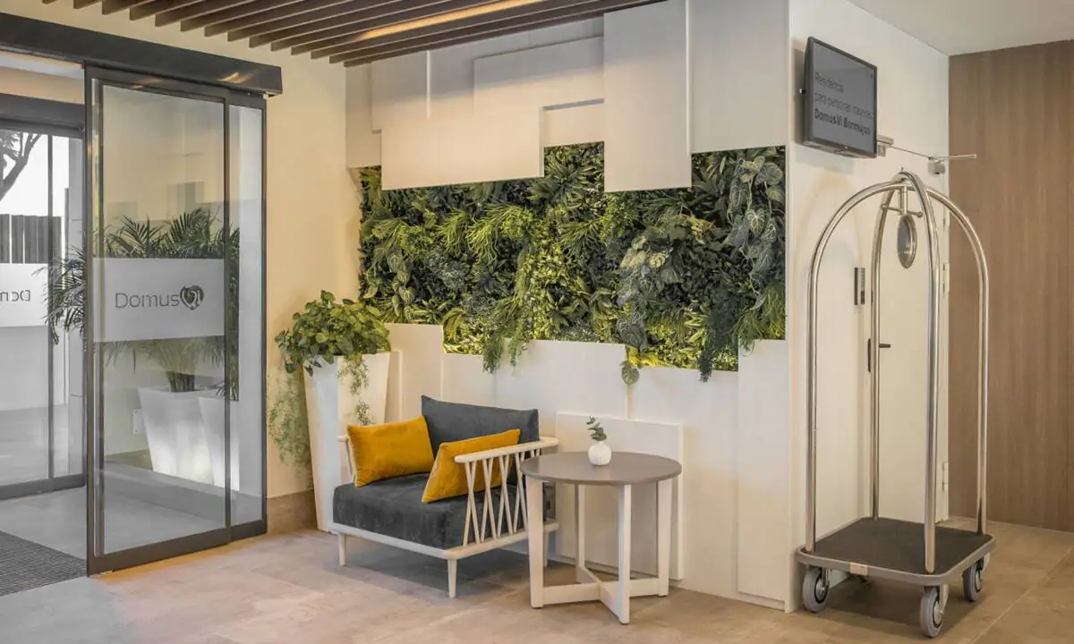 Zona de entrada a residencia de mayores con sofás en azul y amarillo y jardín vertical a medida decorativo
