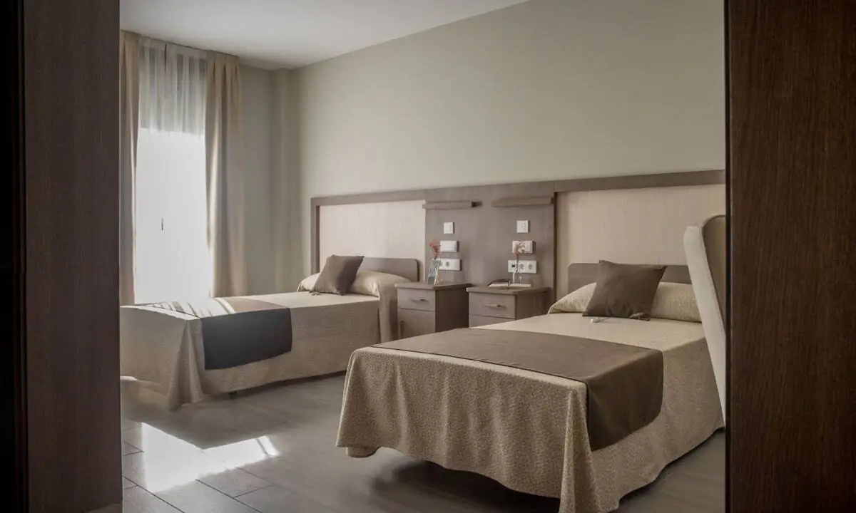 Habitación con dos camas en residencia de mayores con tonos beige y marrón