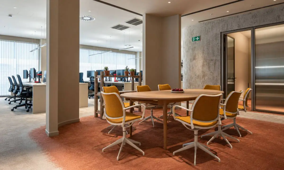 Sala de reuniones abierta en oficina, con zona de puestos operativos de trabajo individual